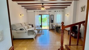 Uma sala de estar ampla, com teto de madeira, um sofá, uma mesa de jantar e uma escada.