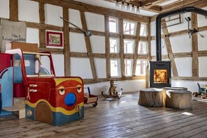 Ein rustikaler Raum mit freiliegenden Holzbalken, einem Kamin, einem bunten Spielzug und einer alten Waschmaschine.