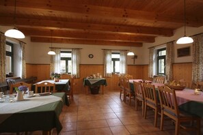 A dining area with wooden tables and chairs, a clock on the wall, and windows with curtains. - Holiday apartment with 2 bedrooms (Geiersthal)
