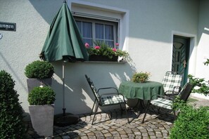 Une terrasse avec une table et des chaises, un parasol vert et des plantes en pot.