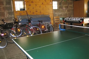 Ein Zimmer mit einem Tischtennisschrank, Fahrrädern und einem Kicker.