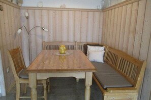 Une pièce comprenant une table en bois, deux chaises, un banc avec des coussins et une lampe.