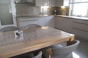 Una cocina moderna con encimera de mármol, electrodomésticos de acero inoxidable y comedor con mesa y sillas de madera.