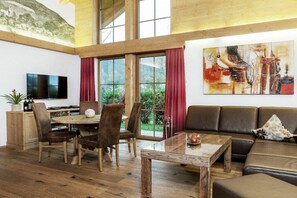 Ein gerÀumiger Wohnbereich mit Holzboden, einem runden Esstisch, einer Ledersofa und einem Bild an der Wand.