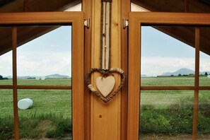 Una puerta de madera con una decoración en forma de corazón, vista a un campo cubierto de hierba y montañas lejanas.