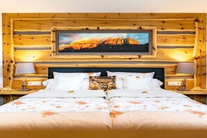 Ein Doppelbett mit floralem Überwurf, ein gerahmtes Bild darüber und Holzvertäfelung an den Wänden.