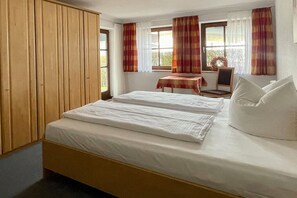 Ein Schlafzimmer mit einem Bett, einem Holzschrank, einem Tisch mit Stuhl und einem Fenster mit Vorhängen.