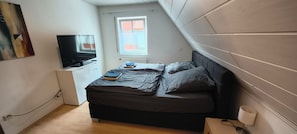 Et soveværelse med en seng, fjernsyn, et vindue og et billede på væggen.