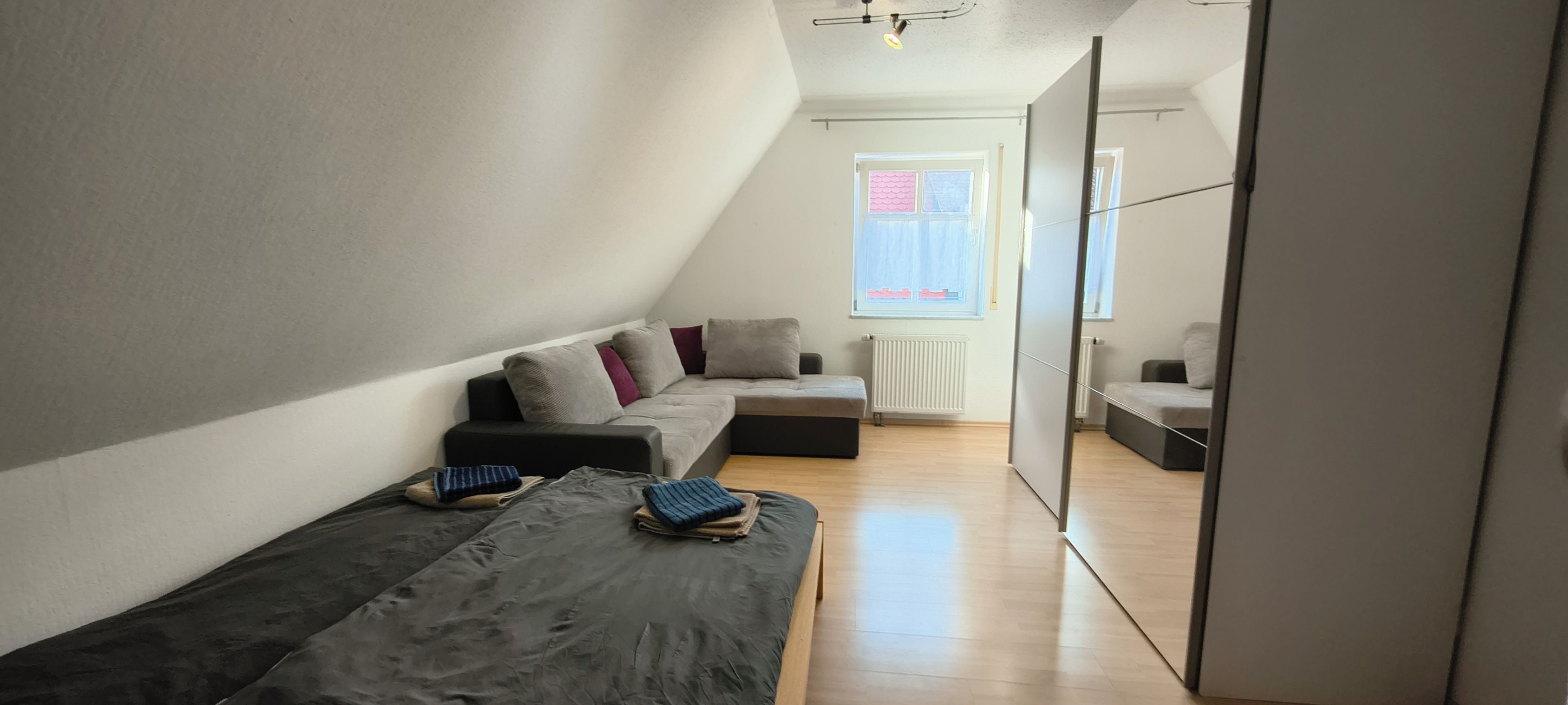 Ein moderner, hell eingerichteter Raum mit einer Eckcouch, einem kleinen Tisch und Blick ins Freie durch ein Fenster.