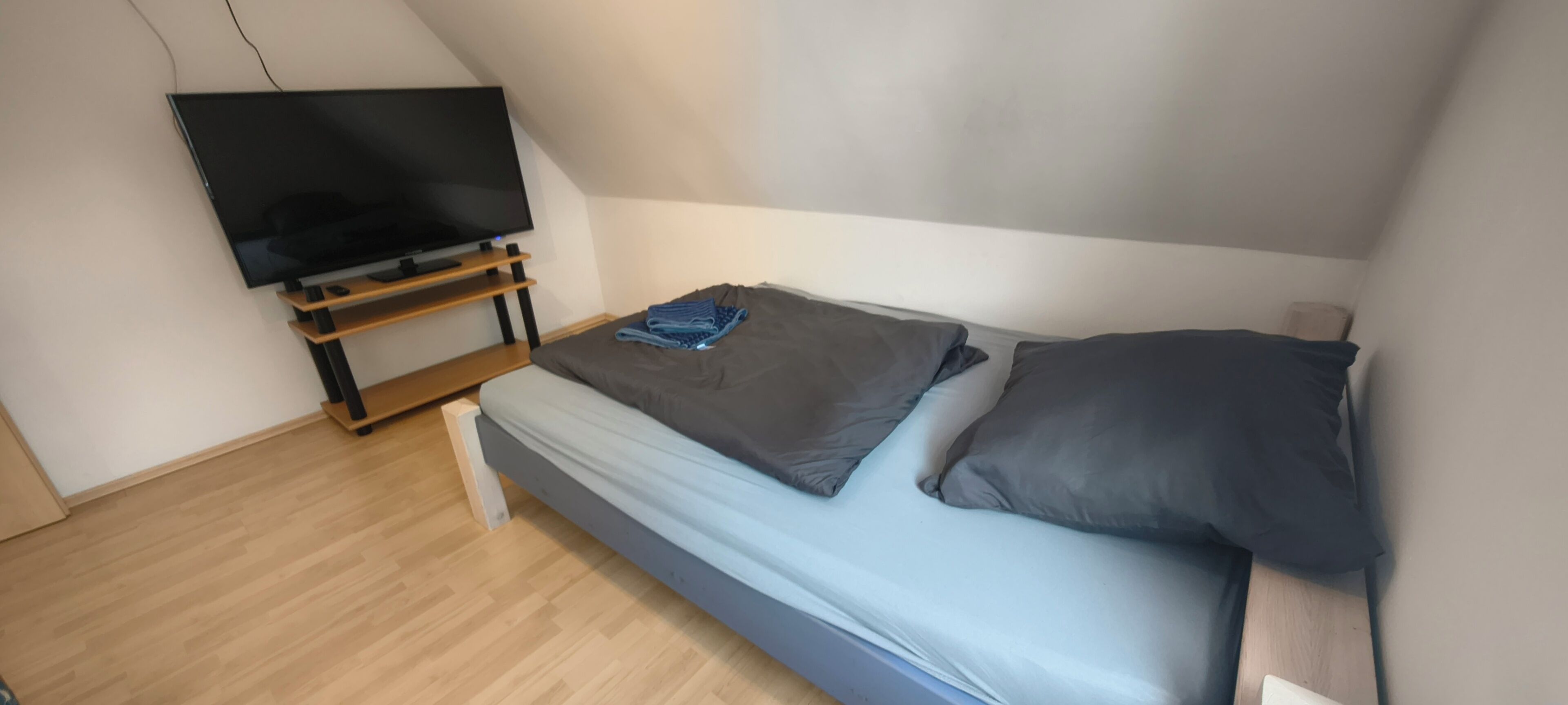 A small room with a bed, a television on a stand, and a wooden floor.