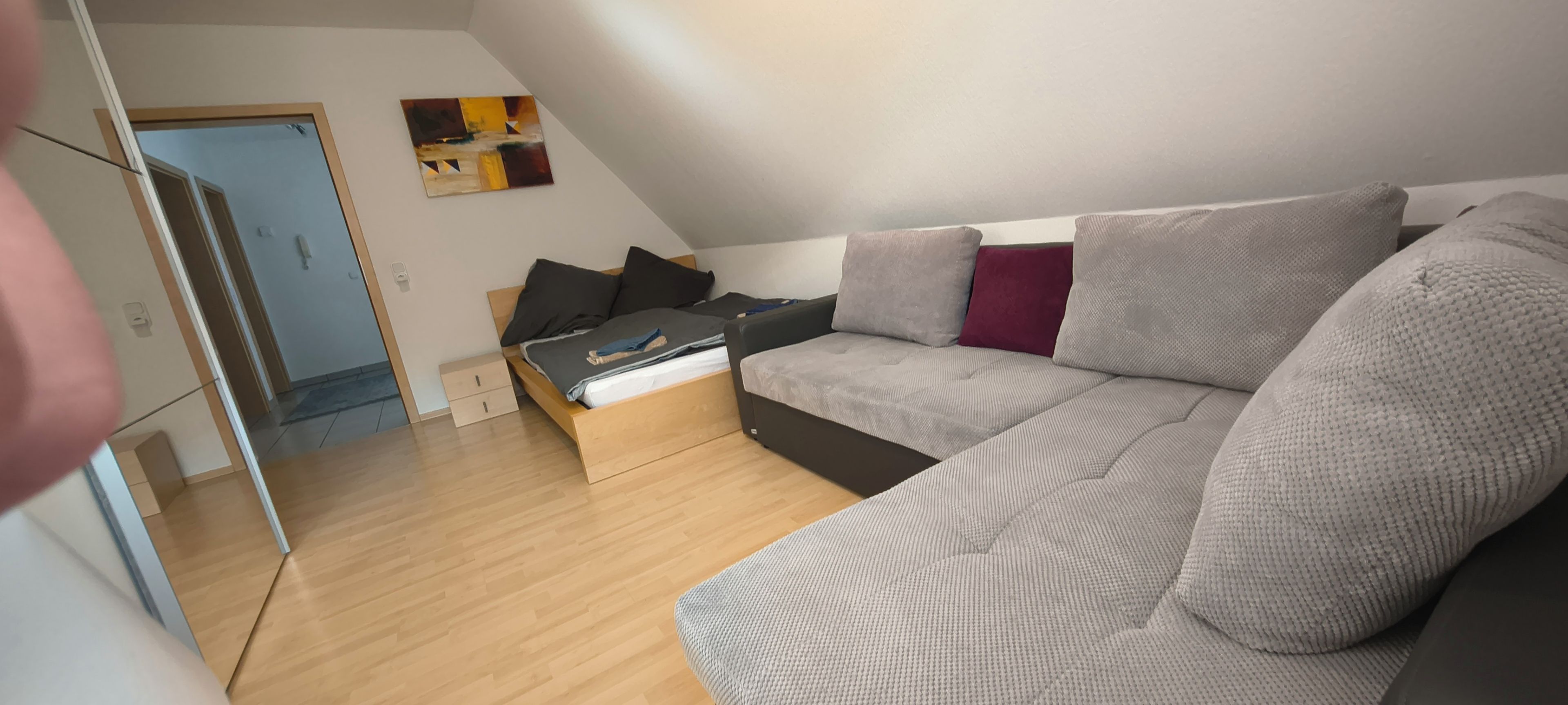 Ett modernt vardagsrum med en grå soffa, ett träbord och en liten säng.