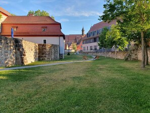Eine grüne Fläche mit Bänken, Steinmauern und traditionellen Gebäuden mit roten Dächern.