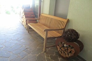 Un banco de madera con una cesta tejida y un montón de leña junto a una pared.