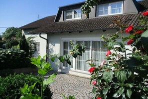 Una casa con techo de tejas, puerta principal con paneles de vidrio y jardín con plantas y flores.