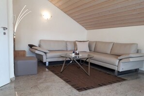 Un salón moderno con un sofá beige, una mesa de centro de cristal y un techo de madera.