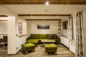 Ein Zimmer mit einem grünen Ecksofa, einem Holztisch und einem Kamin.