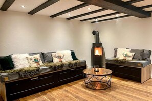 A cozy living room with a fireplace, dark sofas with decorative pillows, and a round coffee table. - Holiday home with 2 bedrooms (Olsberg-Elpe)