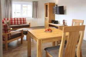 Ein möbliertes Zimmer mit einer Couch, einem Esstisch, Stühlen, einem Fernseher und einem Schrank.