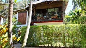 Una casa in legno con un balcone, immersa nel verde e circondata da palme.