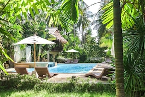 Un área de piscina con sillones de descanso, sombrillas y una estructura de techo de paja.
