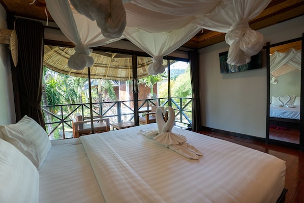 Una habitación de hotel con una cama grande, un balcón con vistas a la vegetación y una cama con dosel.