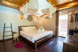 Una cama con dosel impecablemente arreglada, una escalera de madera, un taburete pequeño y un tejido rojo en el suelo.