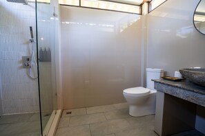 A modern bathroom with a glass-enclosed shower, a white toilet, and a marble countertop with a stone basin. - Garden Chalets (Ko Lanta)