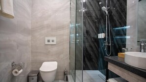 Un baño moderno con cabina de ducha de vidrio, inodoro y lavamanos con encimera de mármol.