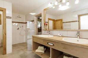 Ein modernes Badezimmer mit zwei Waschbecken, einer Dusche und einem großen Spiegel.