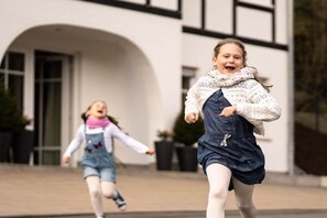Dos niños corriendo hacia un edificio de fachada blanca y marco negro en las ventanas.