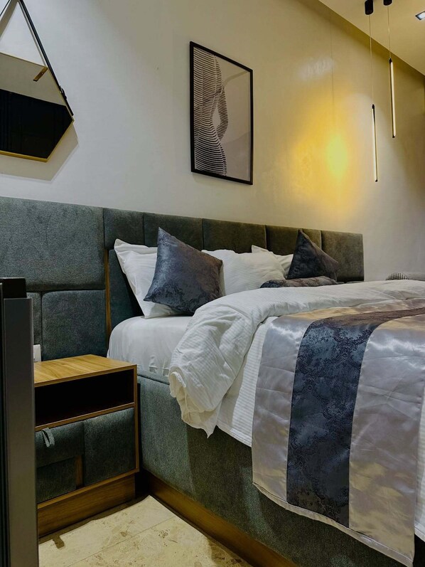 A modern bedroom with a bed, bedside tables, and a wall-mounted artwork.