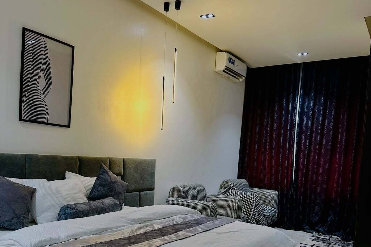 A modern bedroom with a large bed, a headboard, a wall-mounted air conditioner, and a zebra print artwork.