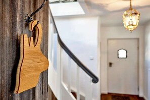 Una decoración con forma de mano de madera colgando de un poste de madera, una escalera con barandilla negra y una puerta con un pequeño ventanal.