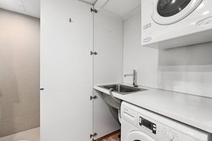 A compact kitchen with a washing machine, a sink, and a door leading to a tiled room. - Poolside Studio Retreat Near Oxford Street (Sydney)