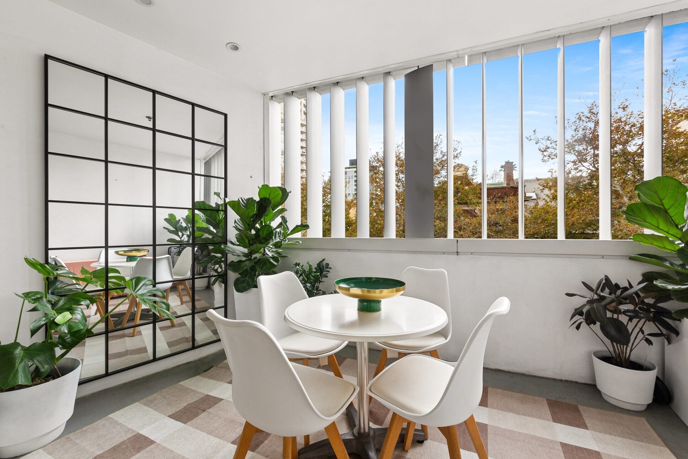 A modern room with a white table, four chairs, a large mirror, and potted plants.