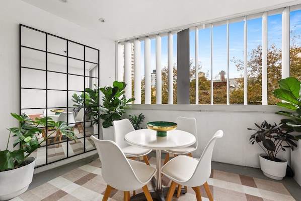 A modern room with a white table, four chairs, a large mirror, and potted plants. - Poolside Studio Retreat Near Oxford Street (Sydney)