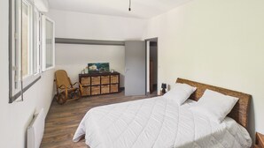 A bedroom with a large bed, wooden flooring, a wicker chair, a small cabinet, and a painting on the wall. - House for 4, enclosed garden – Périgord Noir (Saint-Cyprien)