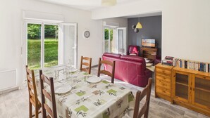 A dining area with a table set for four, a red sofa, a television, and a bookshelf. - House for 4, enclosed garden – Périgord Noir (Saint-Cyprien)