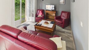 A living room with a red leather sofa, a wooden coffee table, a television, and a red leather armchair. - House for 4, enclosed garden – Périgord Noir (Saint-Cyprien)