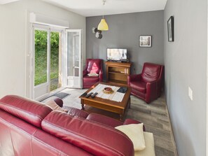 Ein Wohnzimmer mit einem roten Ledersofa, einem Couchtisch aus Holz, einem Fernseher und einem roten Ledersessel.