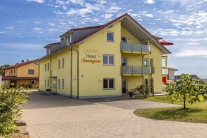Ein gelbes Gebäude mit der Aufschrift 'Haus Sonnenguss', einem überdachten Außenbereich und einem gepflasterten Eingang.