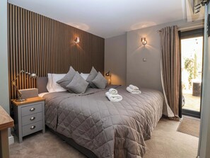 A modern hotel room with a large bed, bedside lamps, a nightstand, and a view through a sliding door. - Blacksmiths Retreat (York)