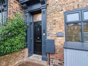 A black door with a brass handle, a brick wall, a green hedge, and a sign reading '50A'. - Blacksmiths Retreat (York)