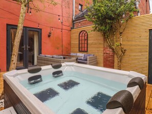 A hot tub in a courtyard with a wicker sofa and a wooden wall. - Blacksmiths Retreat (York)