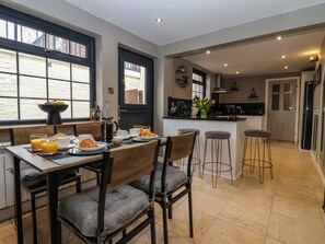 A modern kitchen with a dining area, featuring a breakfast setup with croissants, coffee, and fruit. - Blacksmiths Retreat (York)