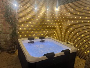 A hot tub with a wooden slatted wall and string lights. - Blacksmiths Retreat (York)