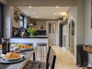 A modern kitchen with a dining area, featuring a central island, bar stools, and a breakfast setup with croissants and orange juice. - Blacksmiths Retreat (York)