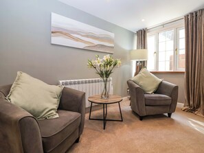 A living room with two sofas, a small table with a vase of flowers, a radiator, and a window with curtains. - Blacksmiths Retreat (York)