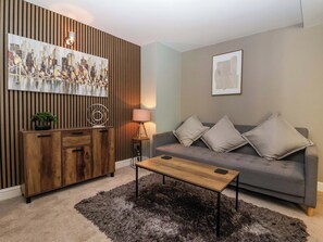 A living room with a sofa, a coffee table, a cabinet, a lamp, and a painting on the wall. - Blacksmiths Retreat (York)