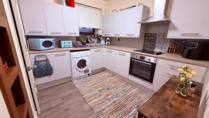 A compact kitchen with a washing machine, oven, and microwave. - Apartment Sleeps 2 With Parking (Aberdeen)
